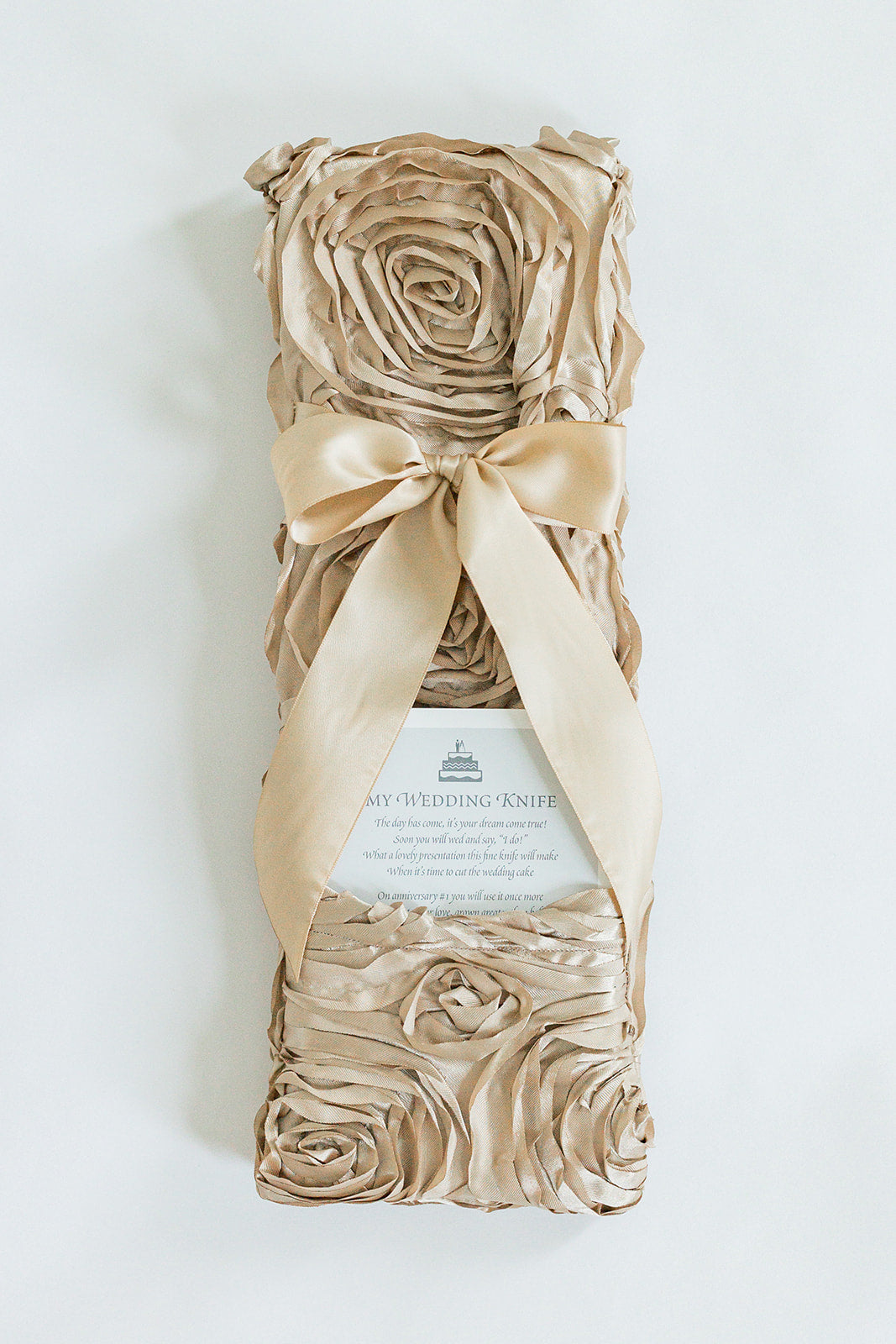 A Rosettes Champagne box by Jubilee Keepsakes, wrapped in champagne-hued fabric roses with a satin ribbon and gift card under the bow, is perfect for presenting the Champagne Wedding Knife.