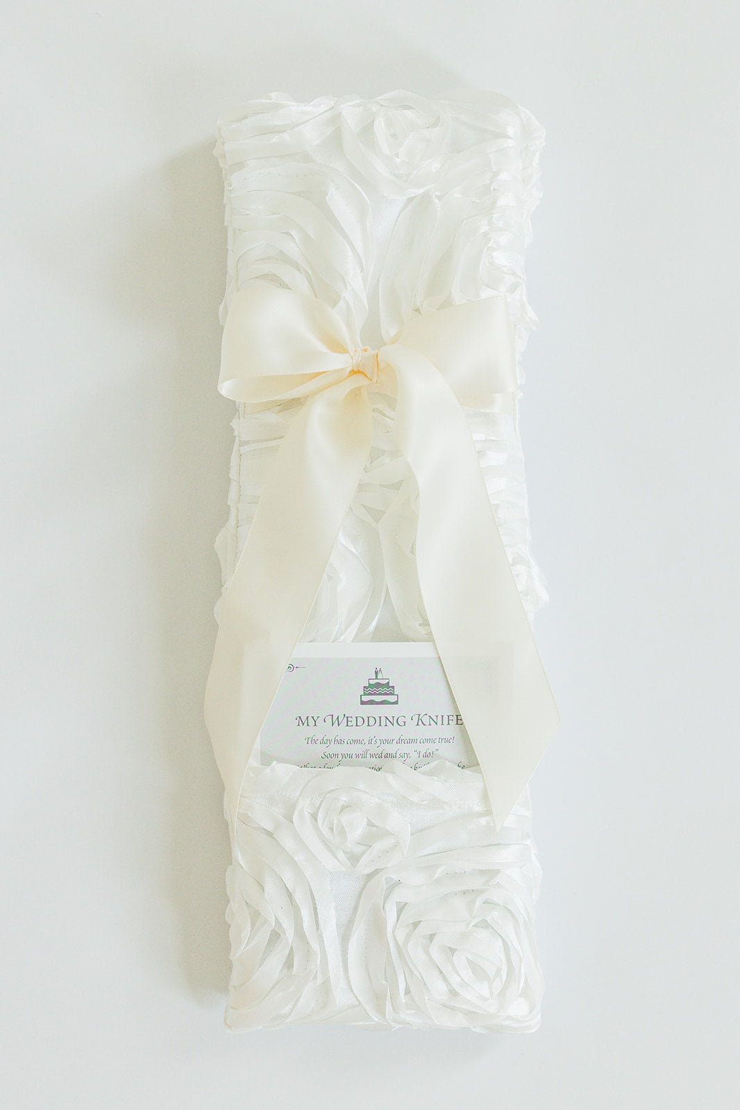 The Rosettes Ivory by Jubilee Keepsakes is a white satin wedding knife holder with rose patterns and a large ivory bow, perfect for your Wedding Knives Collection. Includes a “My Wedding Knife” card for keepsake purposes.
