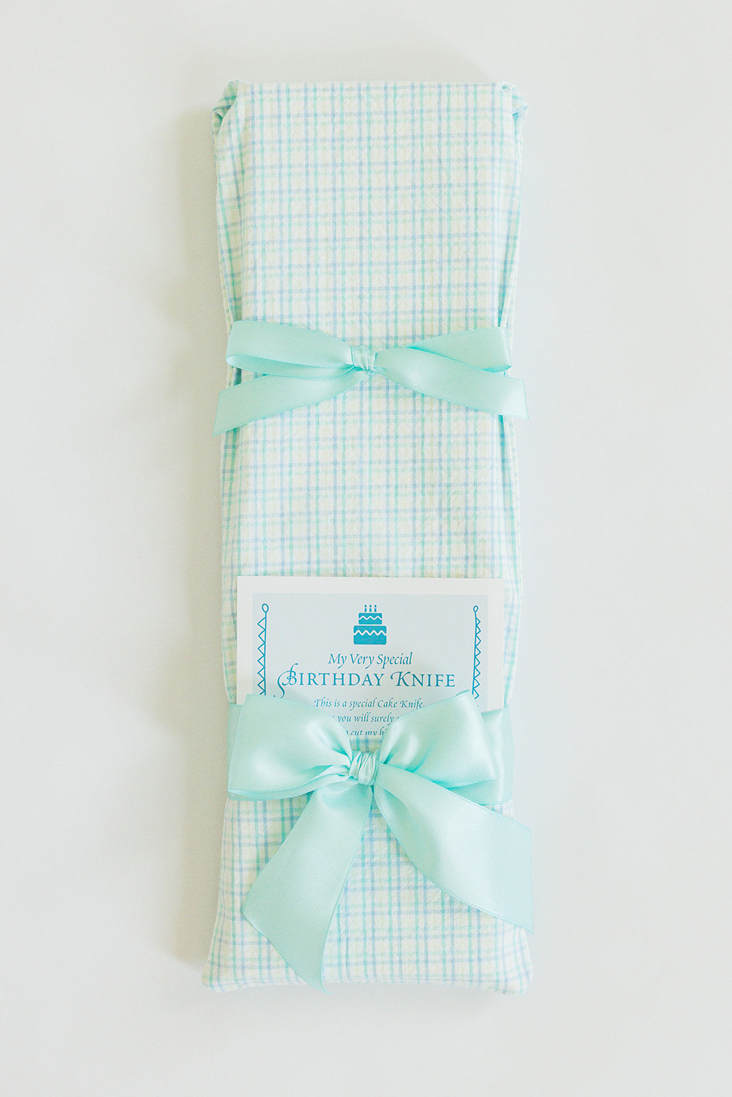 A gift-wrapped package in pastel mint seersucker fabric with a matching pastel mint ribbon by Jubilee Keepsakes—a charming touch for slicing cake and celebrating joyful birthdays.