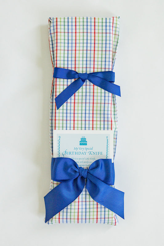 A rectangular gift wrapped in Jubilee Keepsakes' Bright Plaid paper, tied with blue ribbons, and labeled "Birthday Knife," ideal for cake-cutting at birthday celebrations.