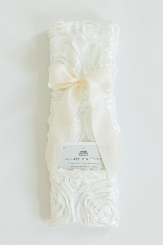 The Rosettes Ivory by Jubilee Keepsakes is a white satin wedding knife holder with rose patterns and a large ivory bow, perfect for your Wedding Knives Collection. Includes a “My Wedding Knife” card for keepsake purposes.